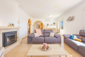 A living room with a fireplace, a grey sofa, a coffee table with decorative items, and a modern light fixture.