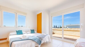 A hotel room with two beds, a balcony with a city view, and a large sliding glass door. - Villa Almendros - PlusHolidays (Calpe)