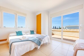 A hotel room with two beds, a balcony with a city view, and a large sliding glass door. - Villa Almendros - PlusHolidays (Calpe)