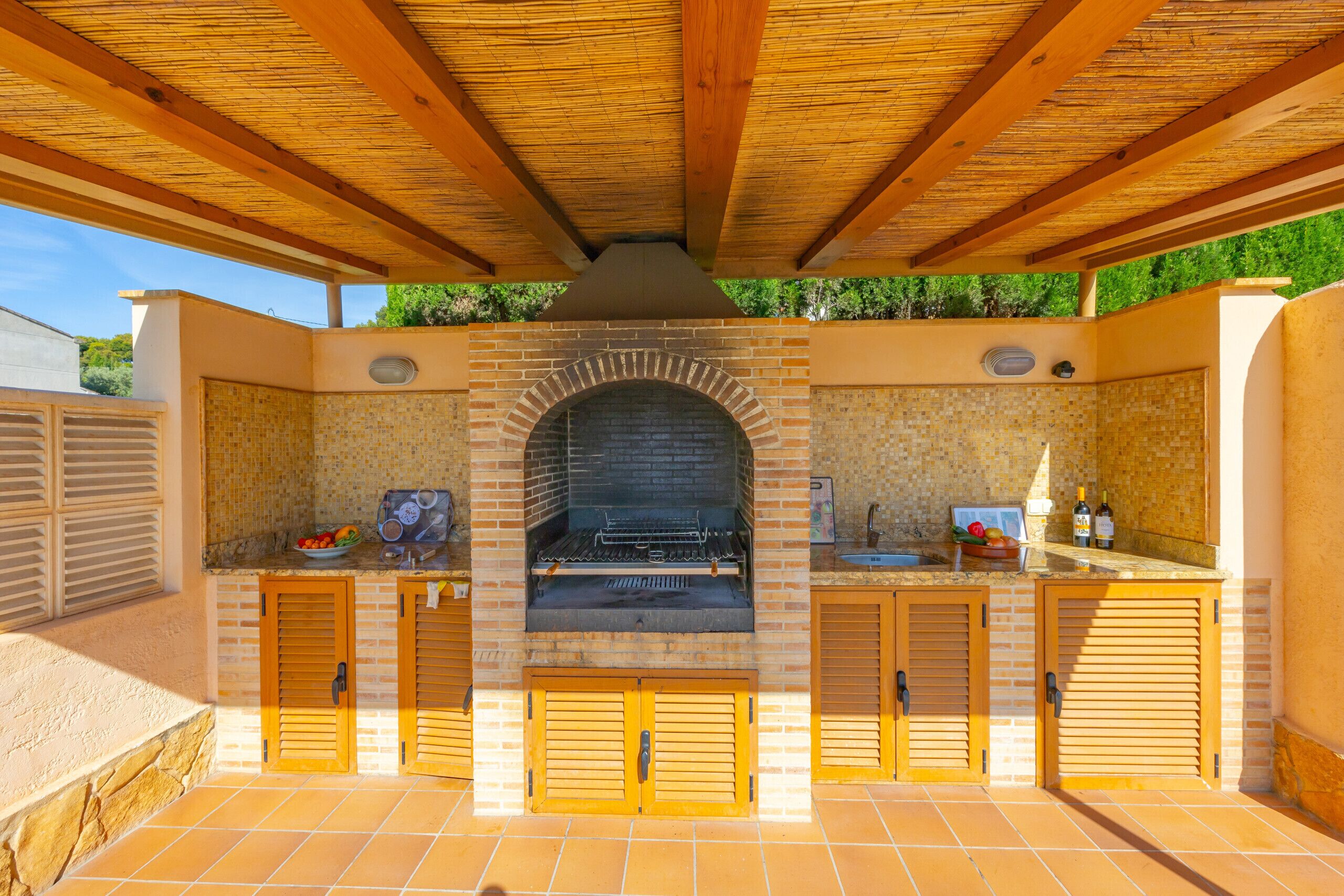 An outdoor kitchen with a brick oven, wooden cabinets, and a tiled floor.