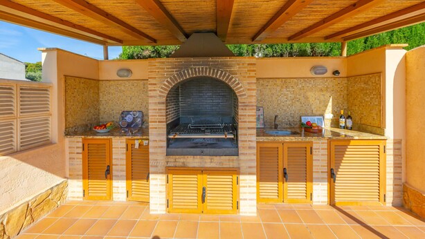 An outdoor kitchen with a brick oven, wooden cabinets, and a tiled floor. - Villa Almendros - PlusHolidays (Calpe)