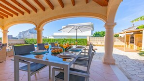 An outdoor dining area with a table set for four, surrounded by white columns, under a wooden ceiling. - Villa Almendros - PlusHolidays (Calpe)