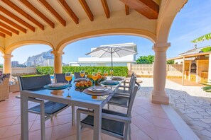An outdoor dining area with a table set for four, surrounded by white columns, under a wooden ceiling. - Villa Almendros - PlusHolidays (Calpe)