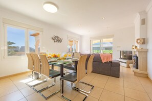 A modern living room with a dining area, a sofa, a TV, and a fireplace. - Villa Almendros - PlusHolidays (Calpe)