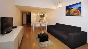 Un salon moderne avec un canapé noir, un téléviseur posé sur un meuble blanc et un coin repas comprenant une table et des chaises blanches.