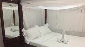Una cama bien hecha con ropa de cama y almohadas blancas, una mesita de noche de madera y un espejo con dosel blanco.