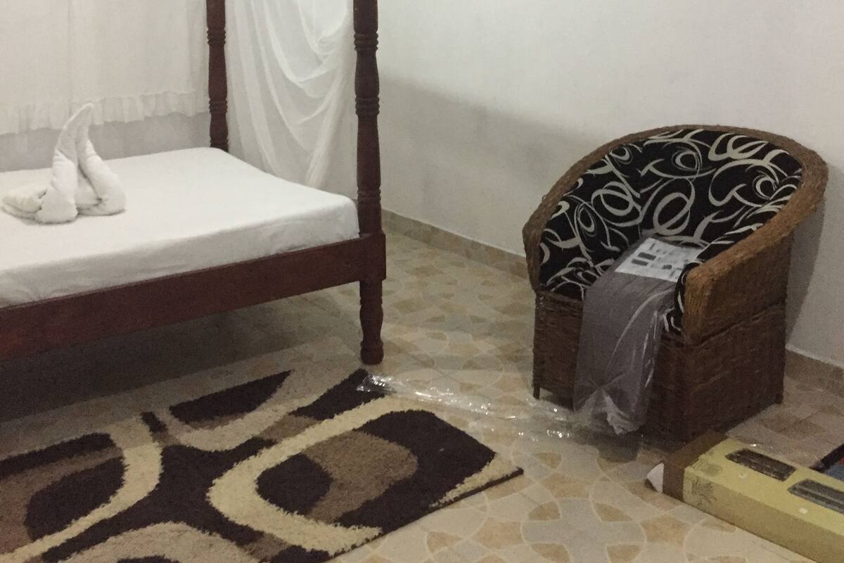 A room with a wooden four-poster bed, a wicker chair, and a patterned rug.
