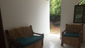 Una habitación con dos sofás de madera tapizados con tela color beige, piso de baldosas y una ventana con reja de metal.