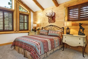 Un dormitorio con cama, paredes de madera, una cabeza de venado montada y una mesita de noche con lámpara.