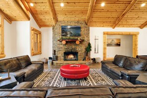 A cozy living room with a stone fireplace, leather sofas, and a patterned rug.
