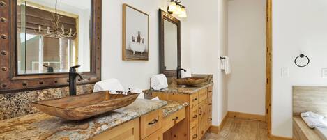 A bathroom with a wooden vanity, a large mirror, a vessel sink, and a shower area.