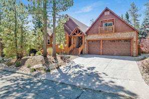 A two-story log cabin with a stone foundation, a wooden deck, and a large garage.