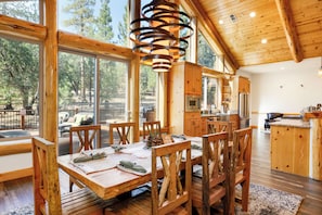 A spacious wooden dining area with large windows, a central wooden table, and a hanging light fixture.