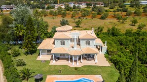 Une grande maison avec une piscine, entourée d’une végétation luxuriante et d’une pelouse bien entretenue.