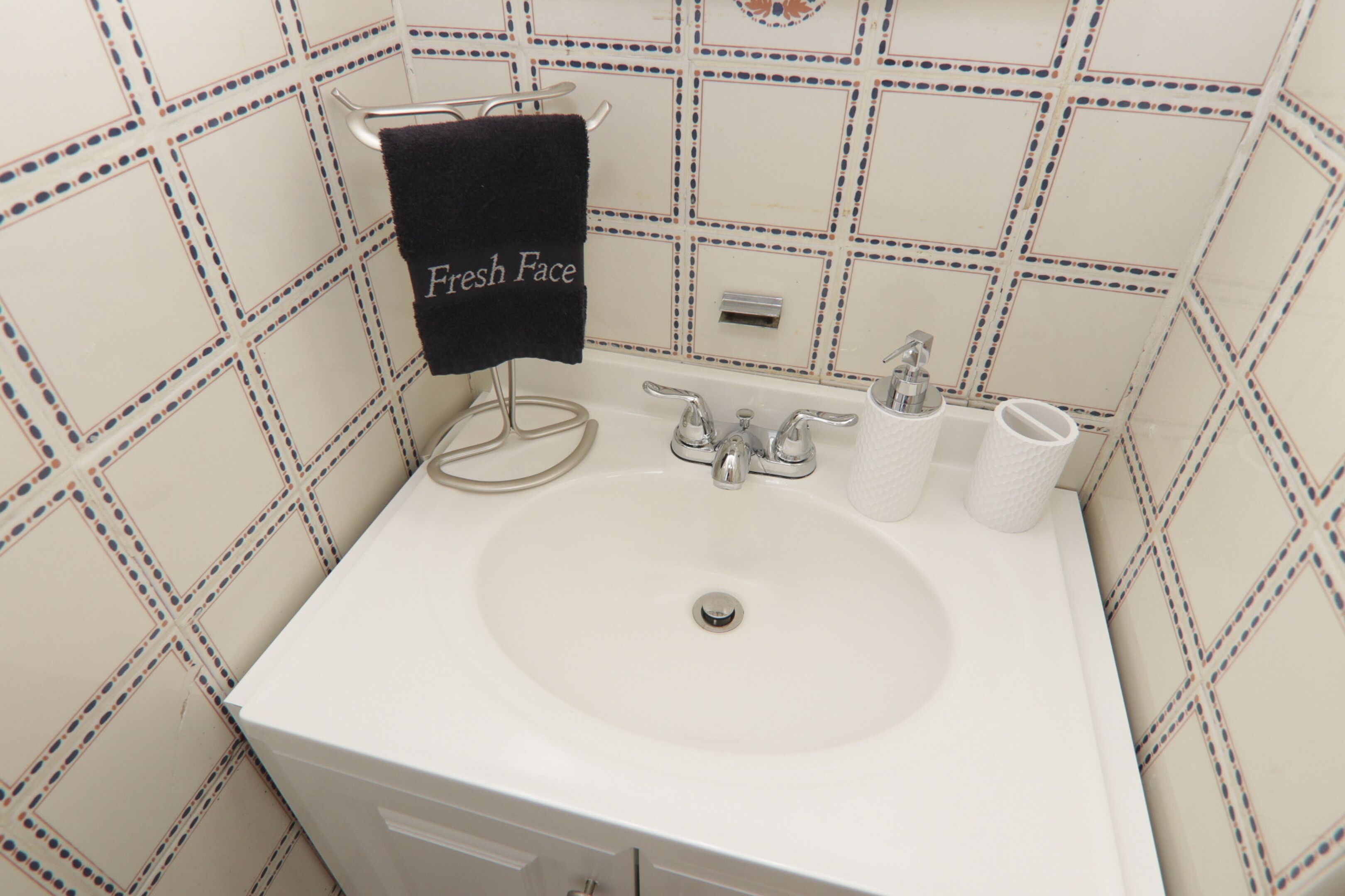 A bathroom with a white sink, two faucets, a towel rack with a towel, and a toilet paper holder.