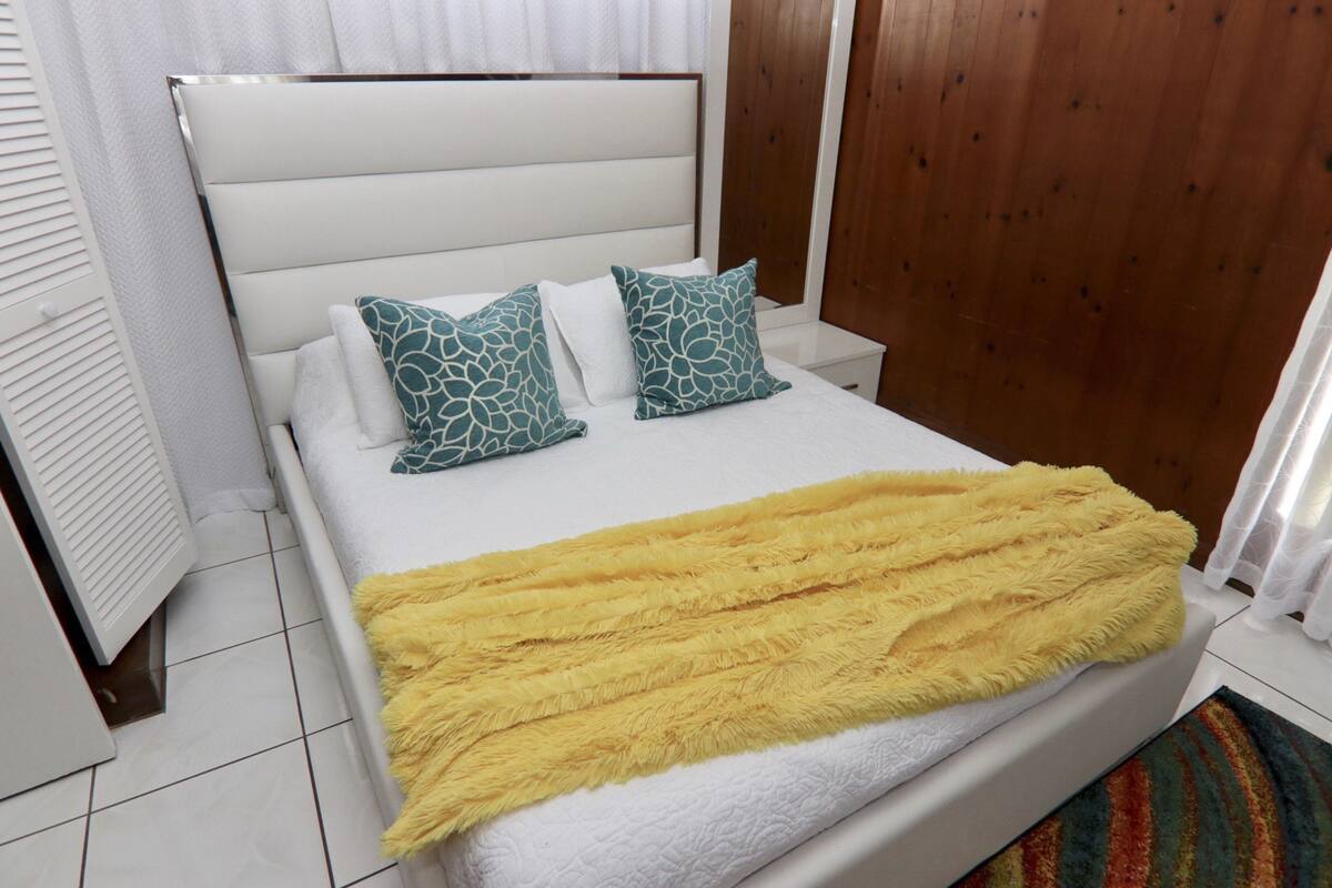 A neatly made bed with a white headboard, two patterned pillows, and a yellow blanket.