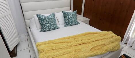 A neatly made bed with a white headboard, two patterned pillows, and a yellow blanket.