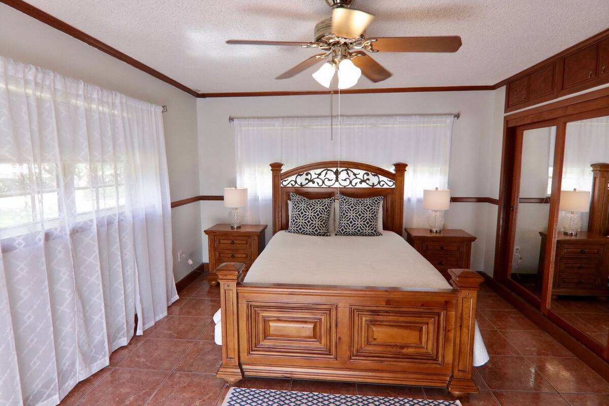 A bedroom with a wooden bed, two bedside tables with lamps, a ceiling fan, and a large mirror.