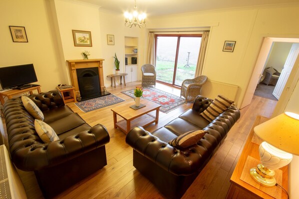 A living room with a fireplace, leather sofas, a television, and a large window.