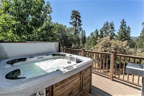 A hot tub on a wooden deck with a wooden railing and trees in the background.