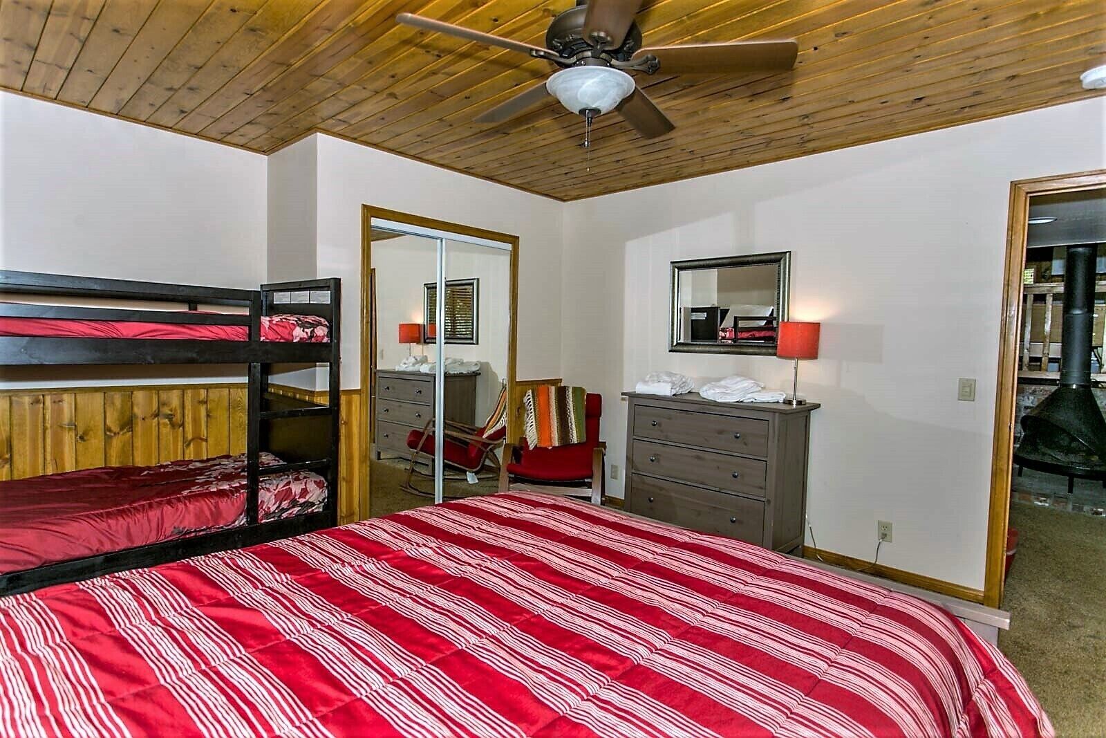 A room with bunk beds, a dresser, a mirror, and a ceiling fan.
