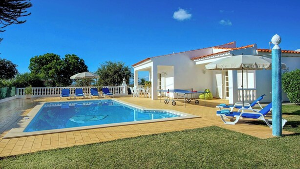 A swimming pool with lounge chairs and umbrellas, surrounded by a white building with a tiled roof. - Villa Licinia - Three Bedroom Villa, Sleeps 6 (Guia)