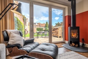 Ein modernes Wohnzimmer mit Ledersofa, schwarzer Lampe, Kamin aus Glas und Blick in den Garten durch große Schiebetüren.