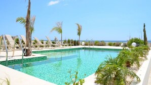 A clear blue pool with lounge chairs and palm trees, overlooking a beach. - Imagine Your Family Renting a Luxury Holiday Villa Close to Sotira’ Main Attractions (Sotira)