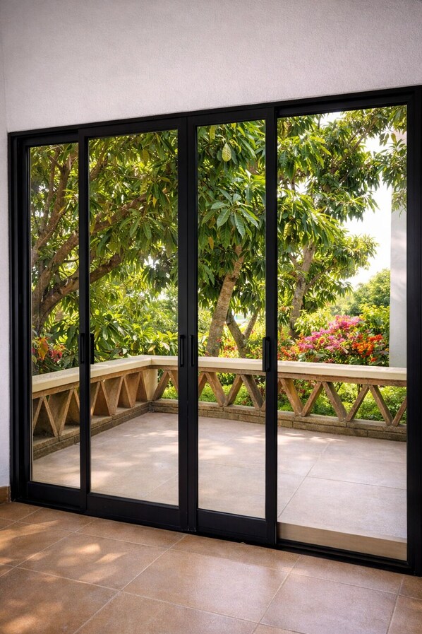 A room with a sliding glass door leading to an outdoor area with a wooden bench and greenery.