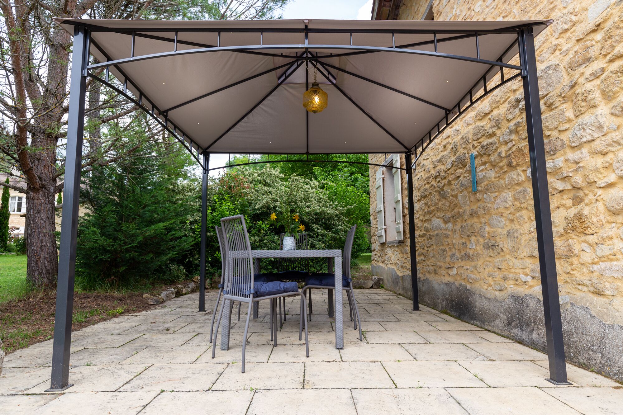 Ein überdachter Patio-Bereich mit Tisch und Stühlen, einer hängenden Leuchte und einer Steinwand im Hintergrund.