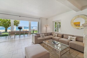 A spacious living area with a large sofa set, a glass coffee table, and a view of the sea through large windows. - VILLA - RIGHT ON THE WATER - LA BOUILLABAISSE BEACH - ST TROPEZ - 14 PEOPLE (Saint-Tropez)