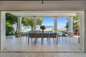 A covered outdoor dining area with a view of the sea and mountains. - VILLA - LES PIEDS DANS L'EAU - LA BOUILLABAISSE BEACH - ST TROPEZ - 14 PEOPLE (Saint-Tropez)