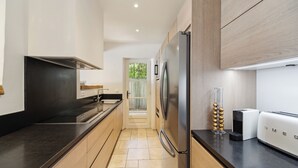 A modern kitchen with a stainless steel refrigerator, a black countertop, wooden cabinets, and a view of a garden through a glass door. - VILLA - LES PIEDS DANS L'EAU - LA BOUILLABAISSE BEACH - ST TROPEZ - 14 PEOPLE (Saint-Tropez)