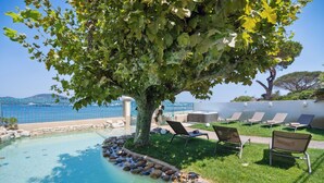 A pool area with a tree, lounge chairs, and a view of the sea. - VILLA - LES PIEDS DANS L'EAU - LA BOUILLABAISSE BEACH - ST TROPEZ - 14 PEOPLE (Saint-Tropez)