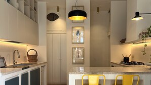 Une cuisine dotée d’un parquet en chevrons, de meubles blancs, d’un îlot central avec des tabourets de bar jaunes et de luminaires suspendus.