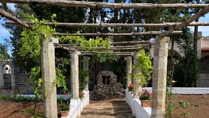 Un chemin de pierres mène à une construction en pierre surmontée d’une pergola en bois.