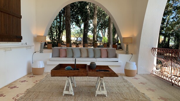 Un espace extérieur accueillant avec un canapé blanc, des coussins à rayures et une table basse en bois.