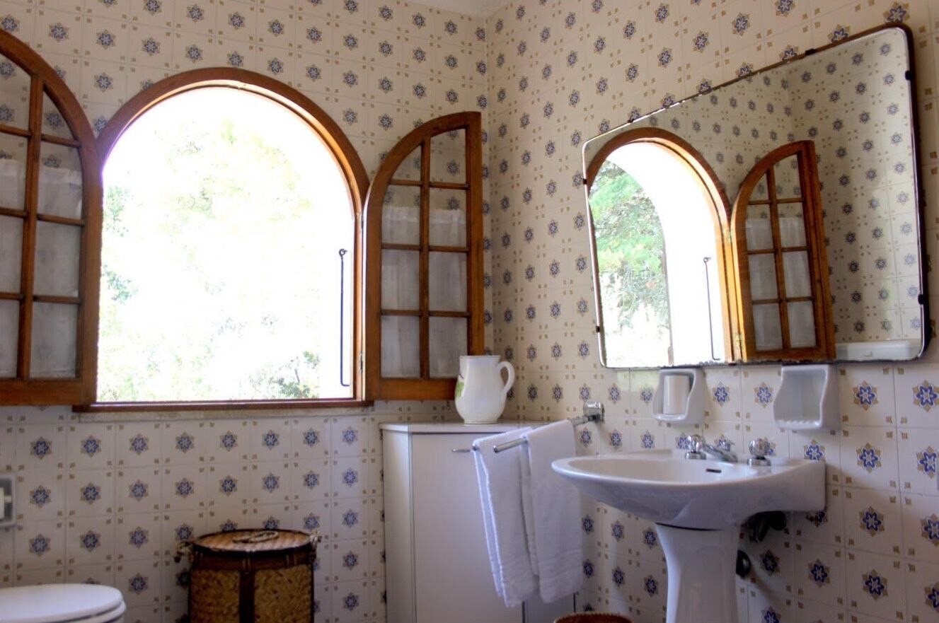 Une salle de bain avec un papier peint à motifs, un lavabo, un miroir et une fenêtre avec des cadres en bois.