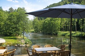 A riverside patio with wicker furniture and a large umbrella.