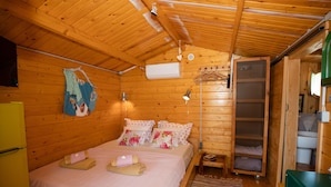 A wooden cabin room with a bed, a small table, a hanging light, and a green cabinet.