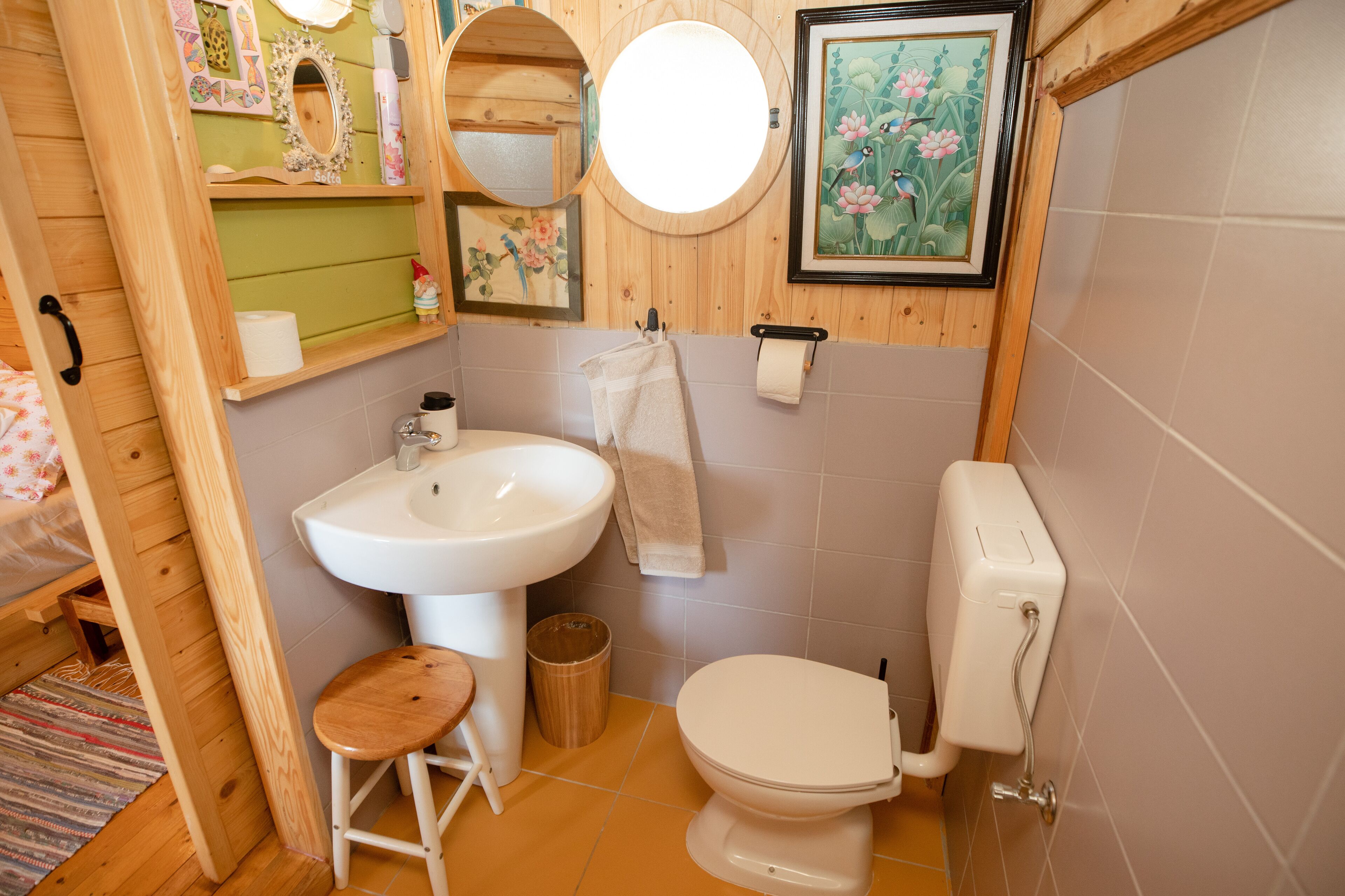 A compact bathroom with a wooden vanity, a sink, a toilet, and a small stool.