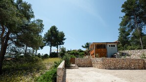 A modern house with a stone wall and a wooden door, surrounded by a gravel driveway and pine trees.