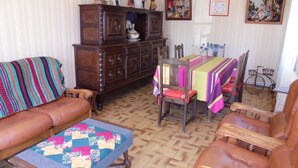 Een woonkamer met een bank, een houten kast, een eettafel met stoelen en een kamerbreed tapijt met een patroon.