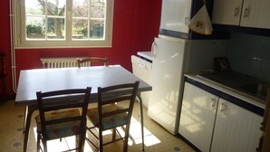 Een keuken met een witte koelkast, houten stoelen, een tafel en kastjes.
