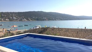 Una piscina con un muro in pietra e vista sul mare e sulle colline.