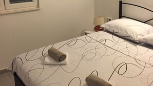 Un letto rifatto con cura, asciugamani arrotolati, un quadro appeso al muro e una finestra con persiane.