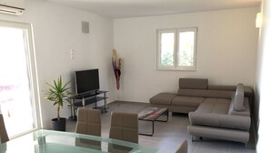 Un soggiorno moderno con un tavolo da pranzo in vetro, un divano, una TV e una pianta in vaso.