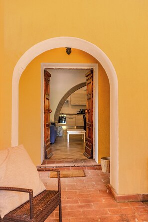 Un arco d'ingresso conduce a una cucina con pavimento piastrellato e una sedia in vimini con cuscino.