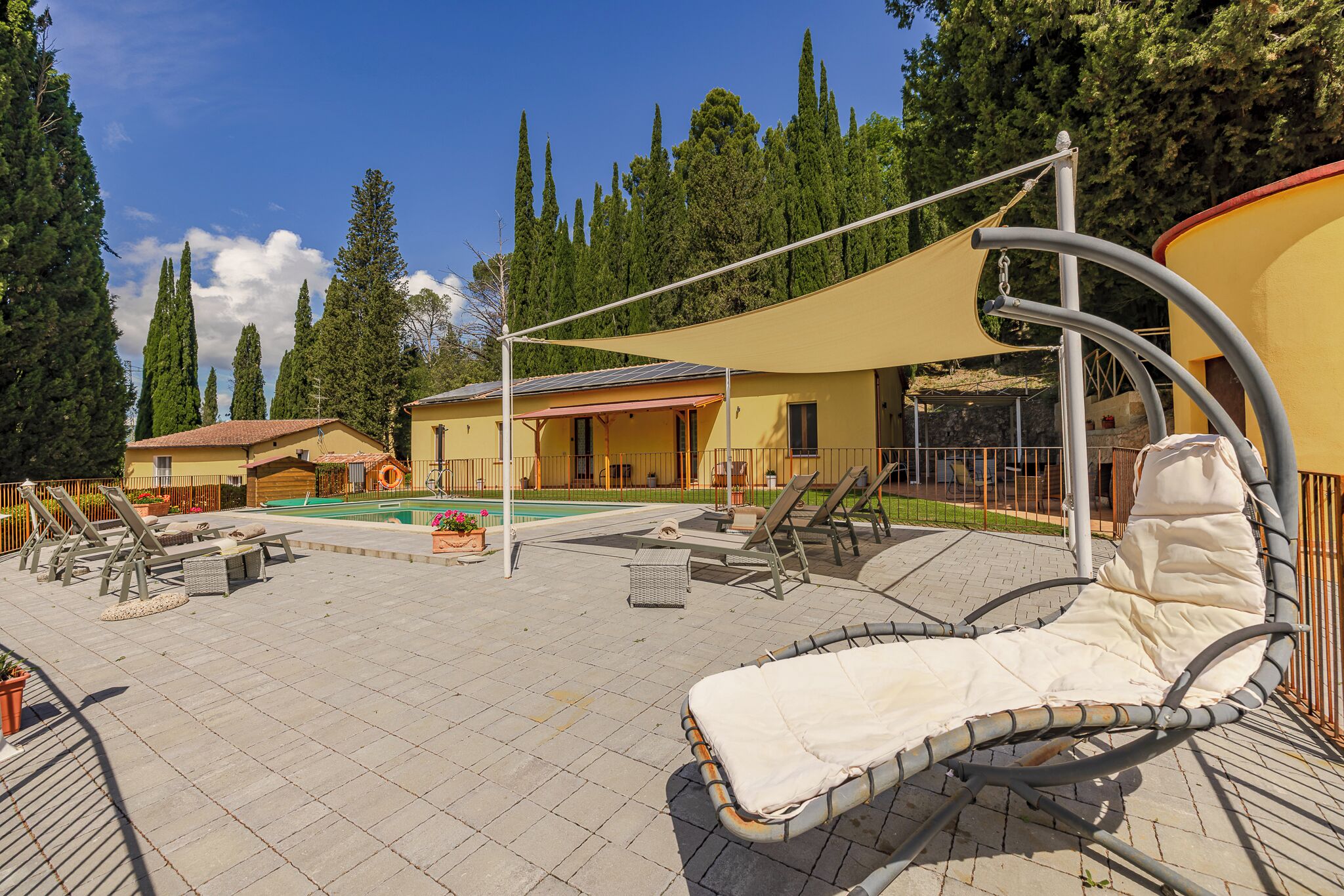 A pool area with lounge chairs, a shaded area, and a building with a tiled roof.