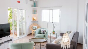 Uma sala de estar moderna com televisão de tela plana, um sofá, uma poltrona, uma mesinha e um abajur decorativo.